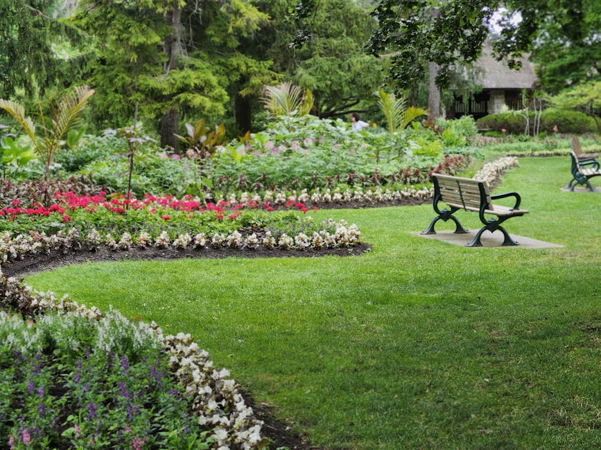 A vibrant garden scene featuring a well-maintained lawn with lush, evenly cut grass in the foreground. Behind the lawn, there is a flower bed densely populated with blooming tulips in shades of purple